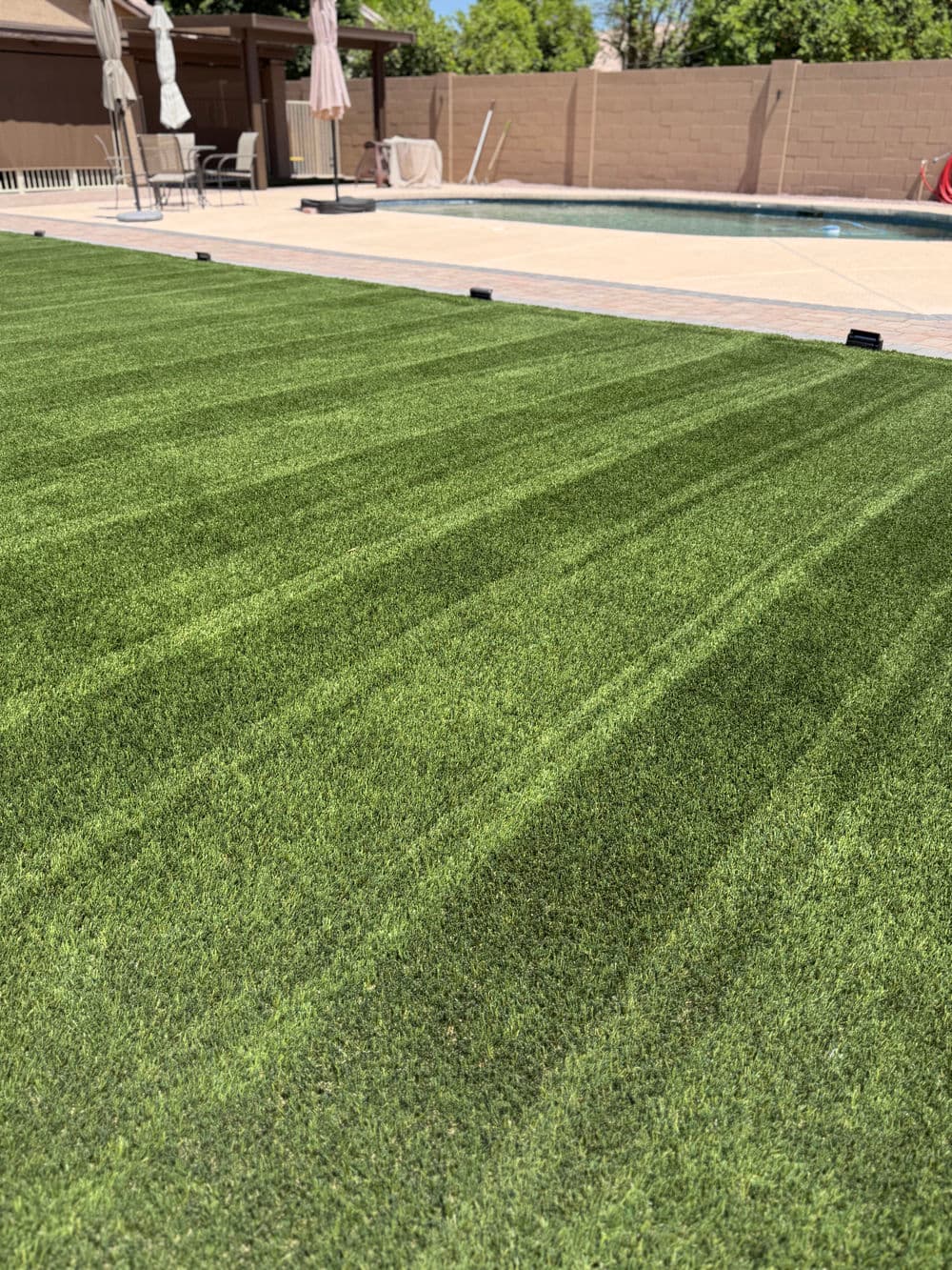 Lush green artificial grass lawn beside a pool with patio seating and umbrellas.