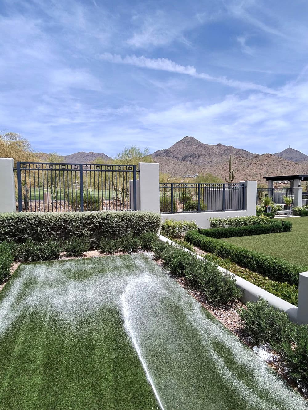 Desert landscape with green lawn, mountains, and a decorative gate under a blue sky.