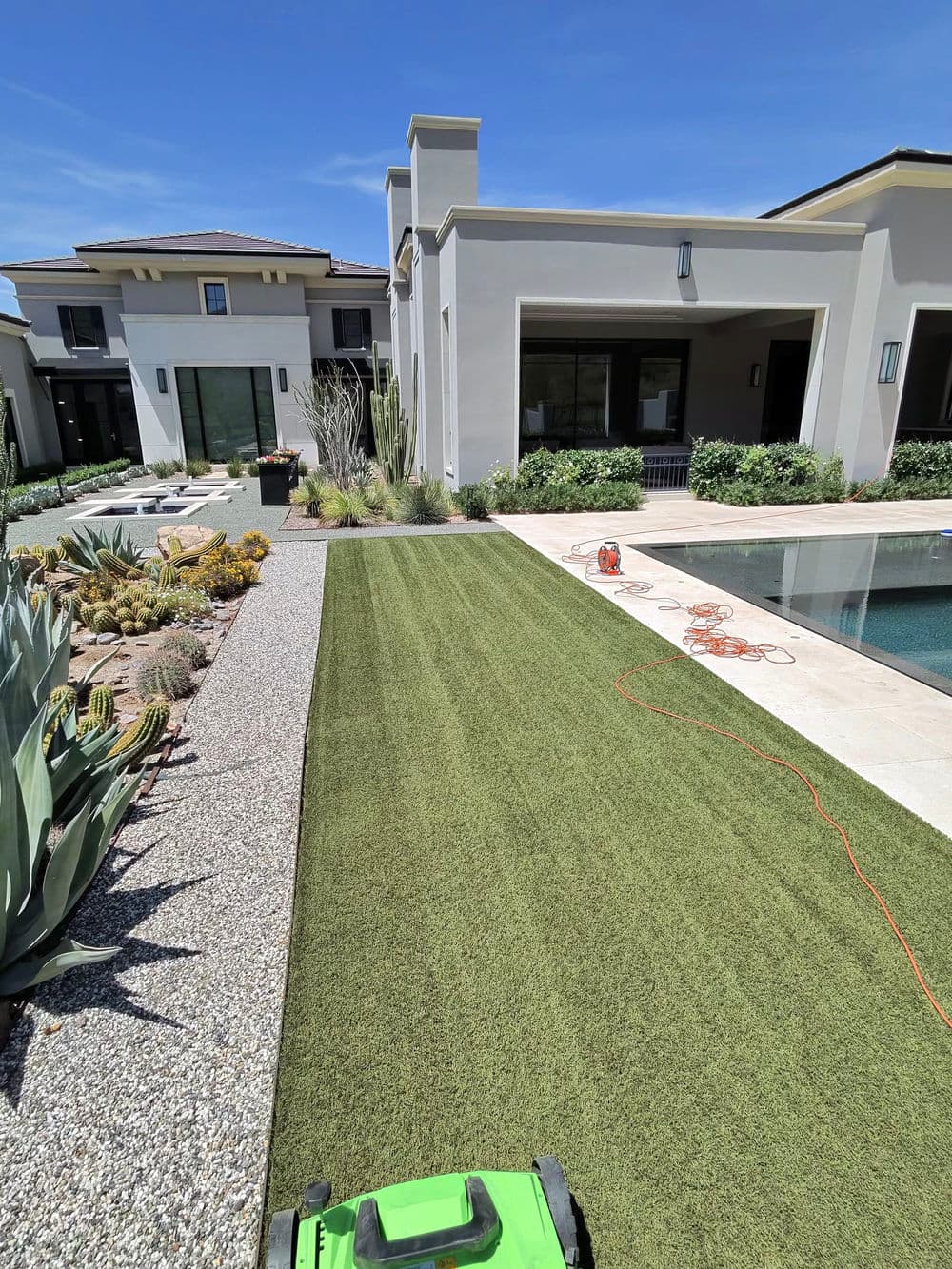 Artificial grass installation alongside a modern house with a pool and desert landscaping.